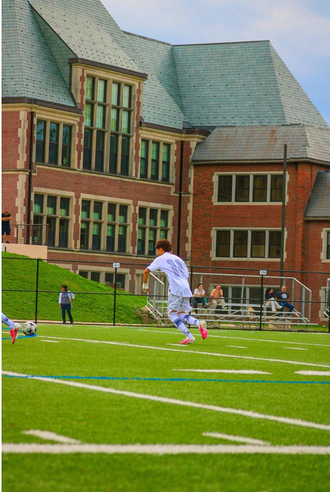 Player 17 in white running toward the ball in front of a brick campus building