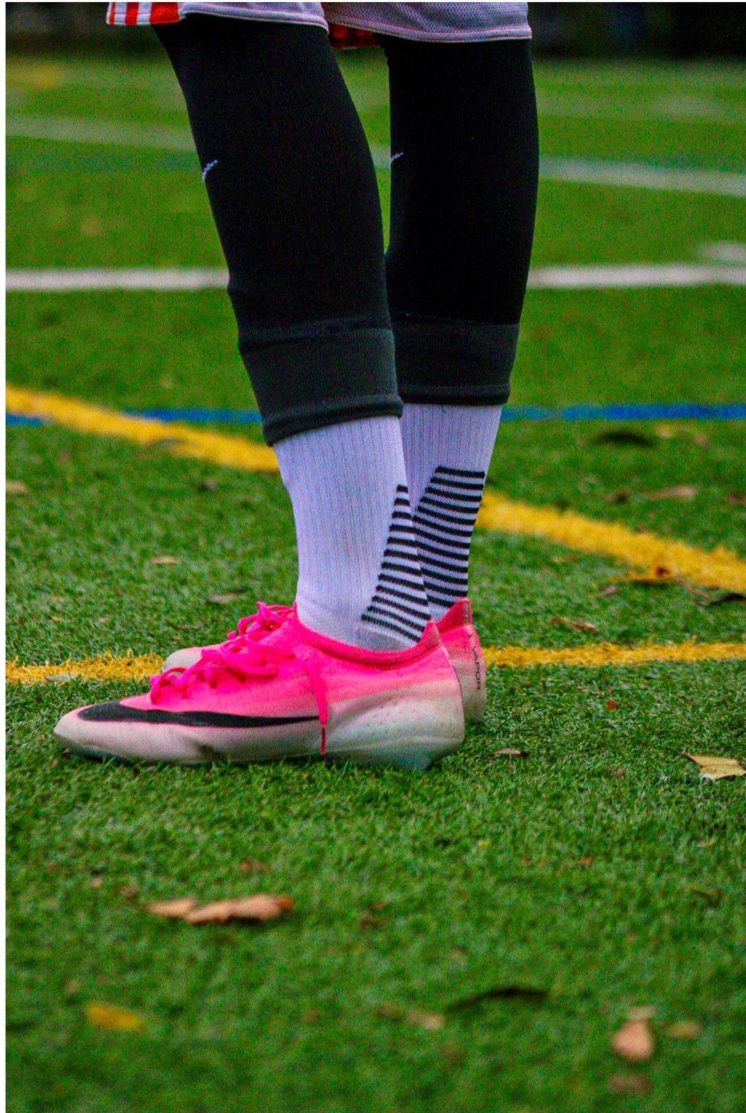 Close-up of neon pink soccer cleats and striped socks standing on green turf