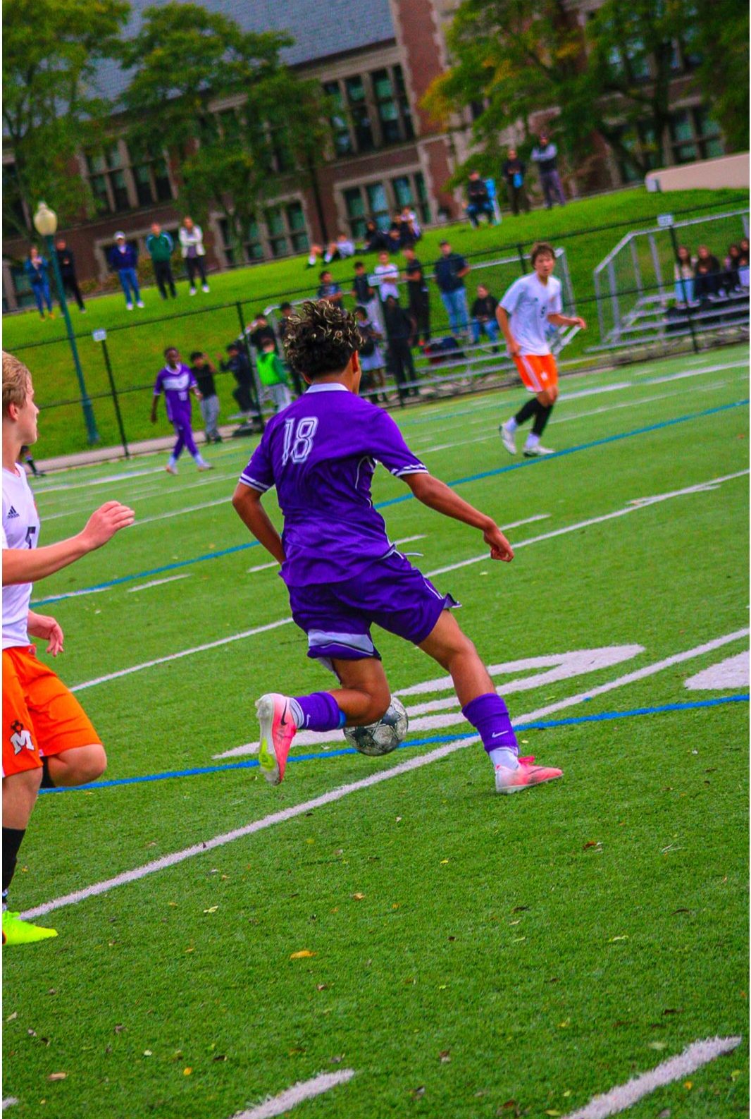 Player 18 in purple driving past a defender in orange and white