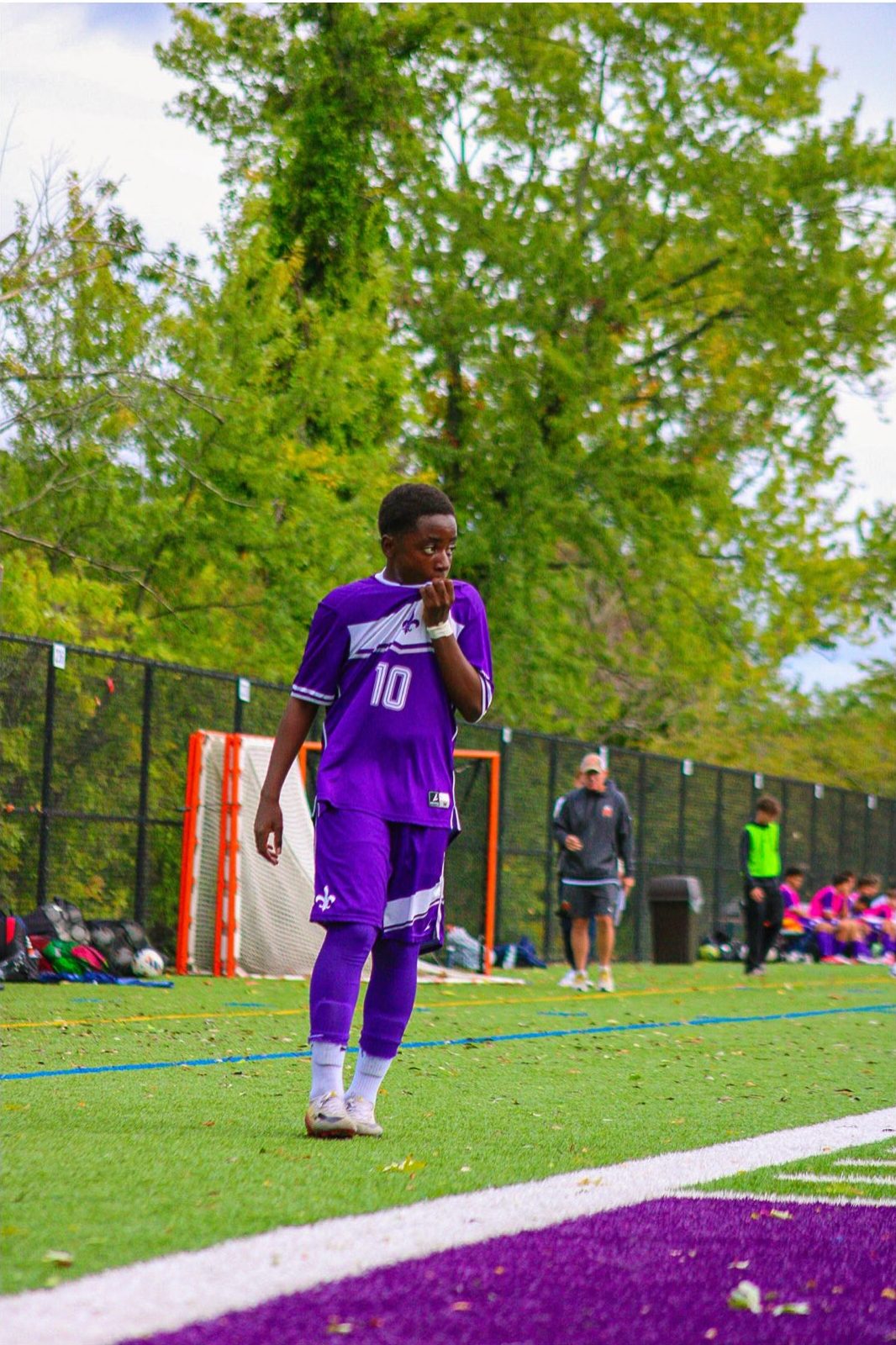 Soccer player in a purple kit walking across the turf with his collar pulled up
