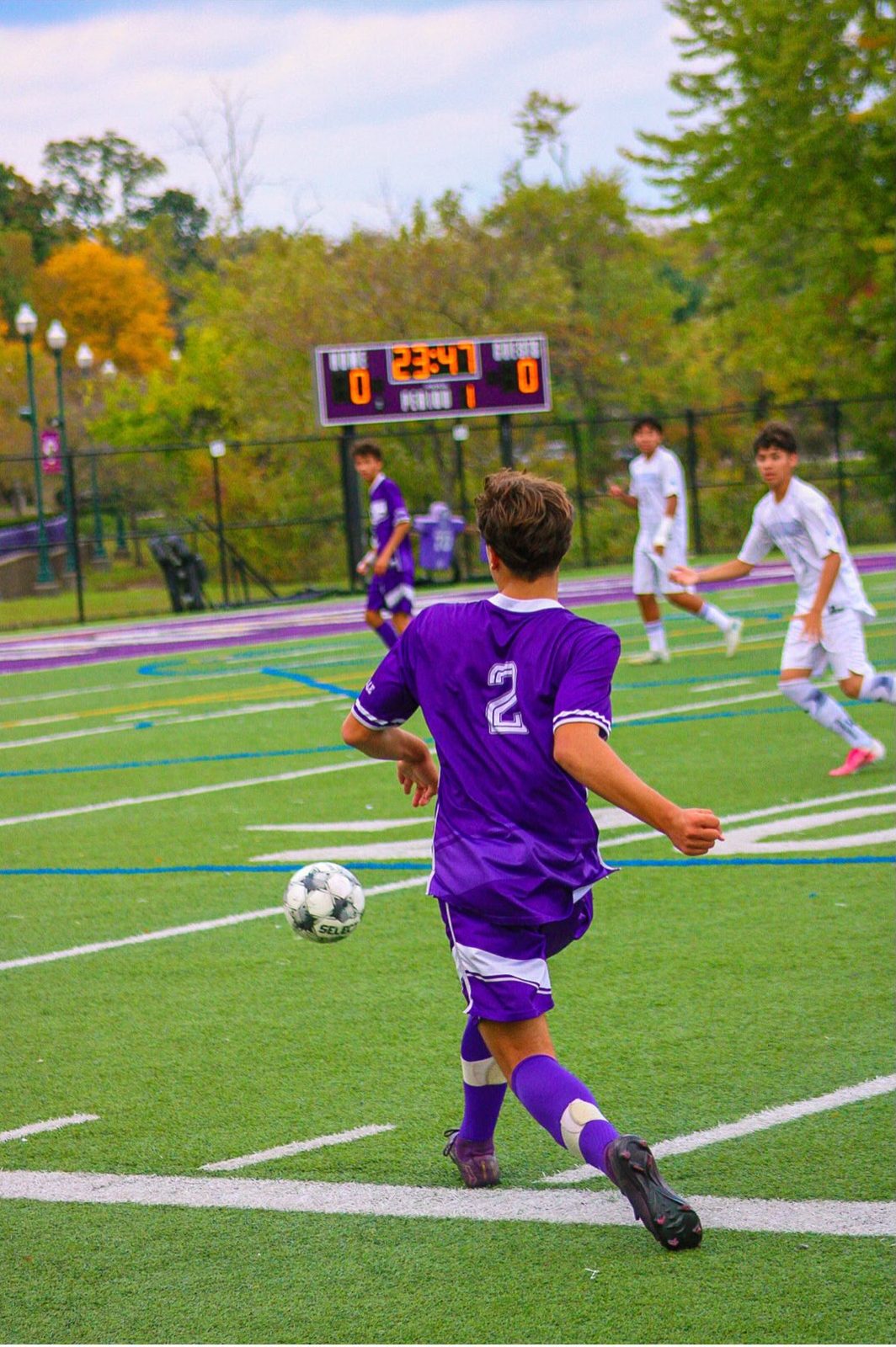 Player 2 playing the ball out from the back as opponents in white close in