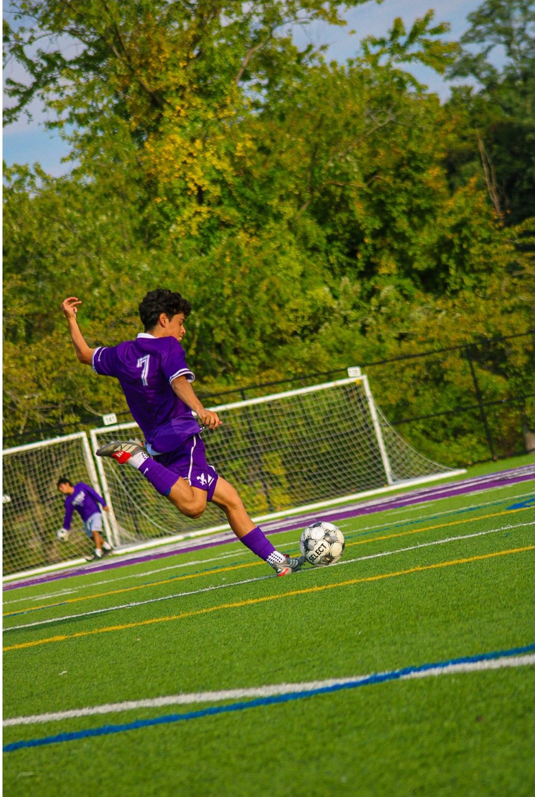 Player 7 in purple swinging through a strike with the goal behind him
